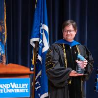 faculty member holds award smiling on stage